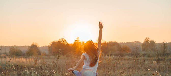 秋天的女孩在田野上享受大自然.户外美容女孩在阳光照射下举起双手.