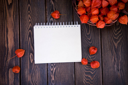 秋天明亮的背景。 铭文的笔记本。 棕色木制背景上的花朵叶子和水果。 秋季假期和感恩节的背景。