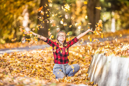 快乐的年轻少女在秋天公园用五颜六色的叶子付钱。