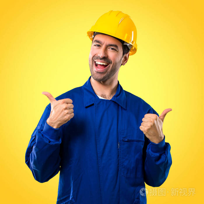 带头盔的年轻工人用双手和微笑竖起大拇指。 黄色背景的欢快表情
