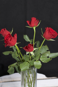 玻璃花瓶里的一束红玫瑰。 五朵花。 在黑色背景上