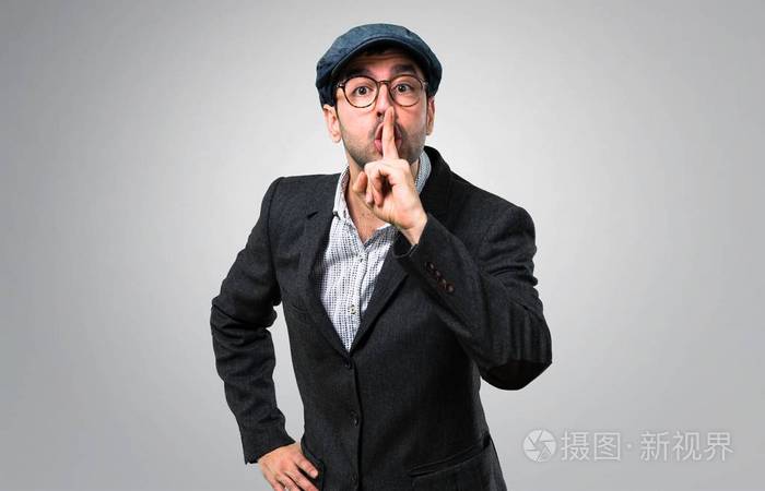 英俊的现代男人,戴着贝雷帽和眼镜,在灰色的背景上表现出闭上嘴和沉默