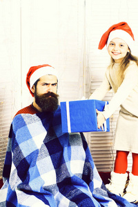 在米色连衣裙可爱微笑金发女郎给长长的胡须，在工作室白色背景上的蓝色格仔格子的圣诞红色帽子的胡子英俊大礼