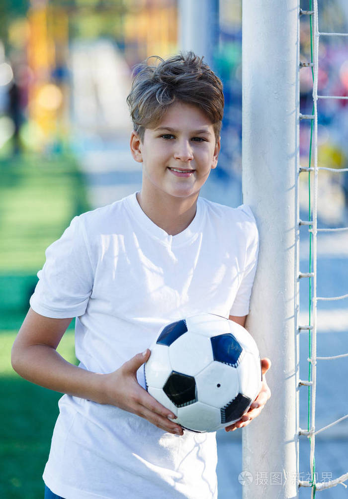 可爱的小男孩穿着白色蓝色运动服在体育场草地上举行古典黑白足球足球