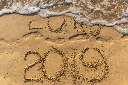 新年理念2019年即将到来，2018年即将离开。沙滩上的文字和沙滩上的脚印。波浪水覆盖数字铭文。在泰国的热带度假胜地见面。