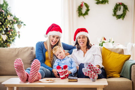 一个小男孩与母亲和祖母在家在圣诞节时间与圣诞老人帽子