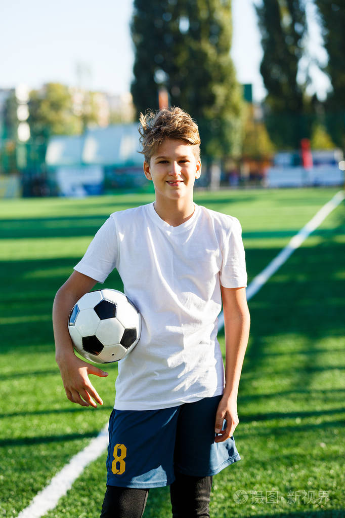 可爱的小男孩穿着白色蓝色运动服在体育场草地上举行古典黑白足球足球