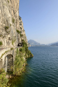 湖畔道路两侧有垂直岩壁的景观，在意大利布雷西亚利蒙附近明亮的落光中拍摄