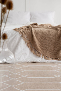 铺有图案的地毯在自然卧室内部，白色床上有棕色毯子。真实照片