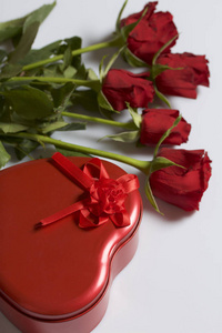 一束猩红玫瑰和一个心形盒子里的礼物。五朵花躺在白色的表面上。