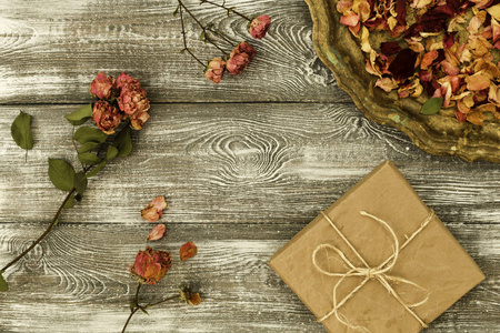 老式托盘与花瓣干燥的玫瑰花礼品盒包装在牛皮纸上的灰色桌子。 平面造型。 文本复制空间