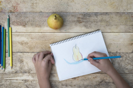 s hands draw a pear with colored pencils. Top view