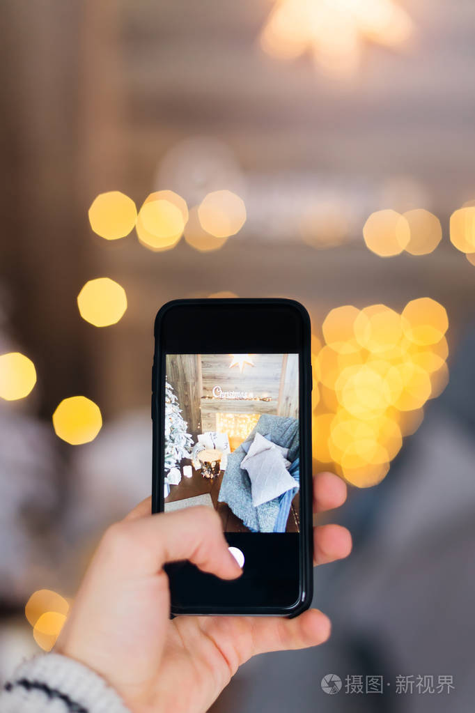 一个手拿着智能手机用圣诞装饰在舒适的房间里拍照的人