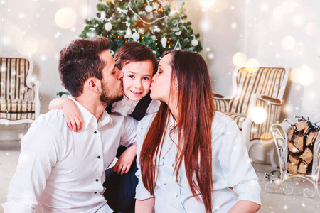 圣诞家庭在圣诞树附近微笑和亲吻。 客厅装饰圣诞树和礼物盒，灯光给人舒适的气氛。 新年主题。 调色
