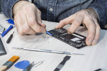 s hand removes the cover of the mobile phone using the tool.