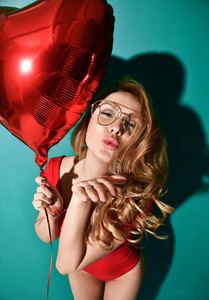 美丽的卷发年轻的妇女在清晰的飞行员眼镜举行大红星气球吹亲吻与嘴唇在薄荷背景的符号