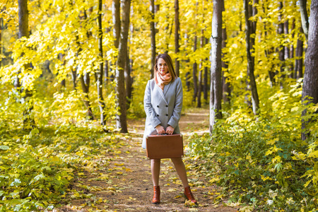 秋天, 季节和人概念迷人的妇女站立与复古手提箱在公园在秋天