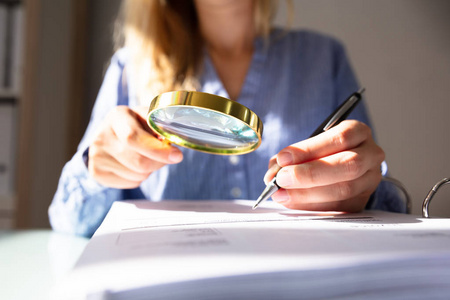 s Hand Checking Invoice With Magnifying Glass Over Desk