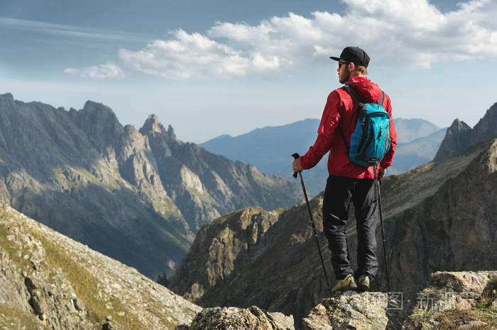 一个戴着太阳镜的胡子男人和一顶带背包的帽子矗立在一块岩石上, 看着