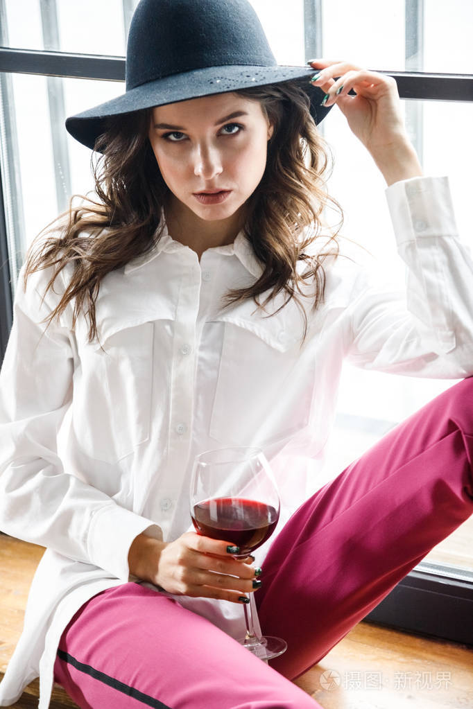 时尚肖像美女黑发模特穿白色衬衫和粉红色裤子在豪华公寓内部摆姿势的