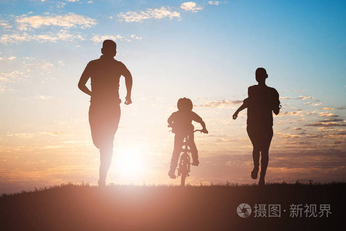 日落时父母带着孩子骑自行车跑步的剪影