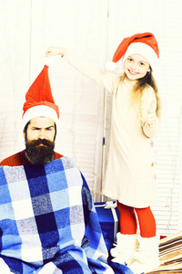 在米色连衣裙可爱微笑的金发女郎在工作室白色背景上的蓝色格仔格子举行绒球的英俊的大胡子男人，留着长胡子的圣诞红色帽子