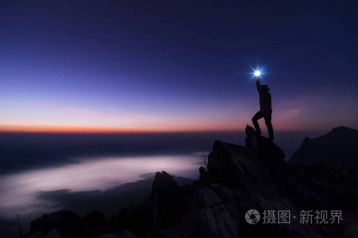 登山者或背包者的轮廓站在岩石山峰和日出成功赢家的概念