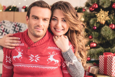 微笑的妻子拥抱丈夫，在家看相机，背景上的圣诞树