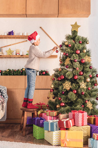 家中圣诞老人礼帽装饰圣诞树的可爱少年儿童侧景