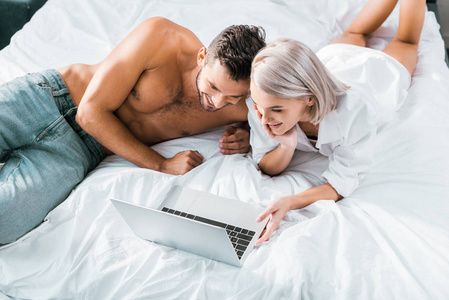 幸福的年轻夫妇在卧室里一起使用笔记本电脑的高角度视角