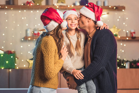 圣诞老人的快乐父母在圣诞节亲吻微笑的女儿