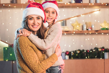 圣诞节时，戴着圣诞帽的母亲和女儿在家拥抱