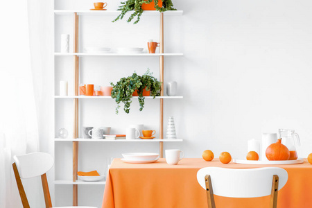 白色木制椅子在桌子上的现代橙色餐厅内部，植物上架。 真实照片