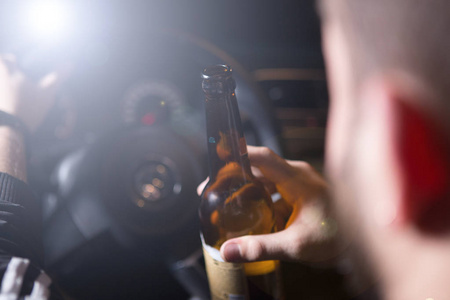 醉酒的年轻男子驾驶一辆带有一瓶啤酒。不要喝和驱动器的概念。影响下驾驶。堆，醉酒驾车。Dwi