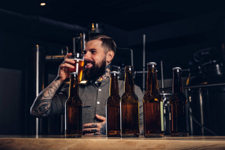 照片与工艺啤酒瓶的前景和胡子男性饮酒的背景