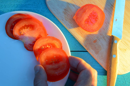 把番茄片铺在盘子上，盘子上放着一块木板，上面放着一张蓝色的绿松石木桌，阳光照耀着