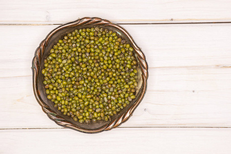 大量的干绿绿豆放在旧铁碗平躺在白木上照片