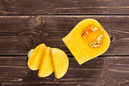 一组四分之一，三片光滑的梨形橘黄色的奶油南瓜，品种扁平，放在棕色的木头上