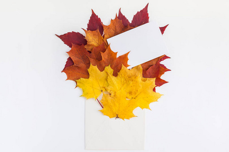 创意顶景平躺秋季概念构图。 信封干燥明亮的秋叶白纸背景复制空间。 模板模拟秋季感恩节结婚纪念日邀请卡