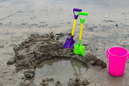 玩具铲子和水桶，海滩上有个洞，靠近