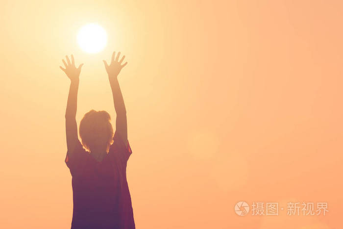 一个女孩的轮廓举起双手对着太阳
