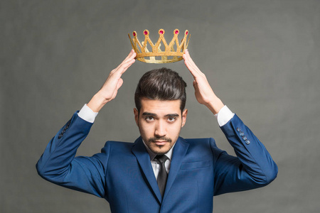 自鸣得意的商人一个穿着蓝色西装,头顶戴着灰色皇冠的年轻帅哥照片