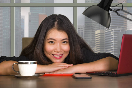 年轻快乐美丽的亚洲企业家女性，在中央商务区的现代办公电脑桌工作，在公司的工作中，成功地坐在窗边