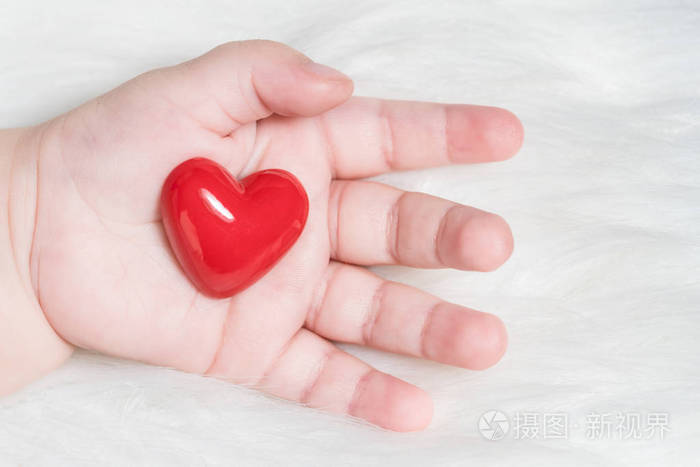 白色毛皮背景下婴儿手中的红心