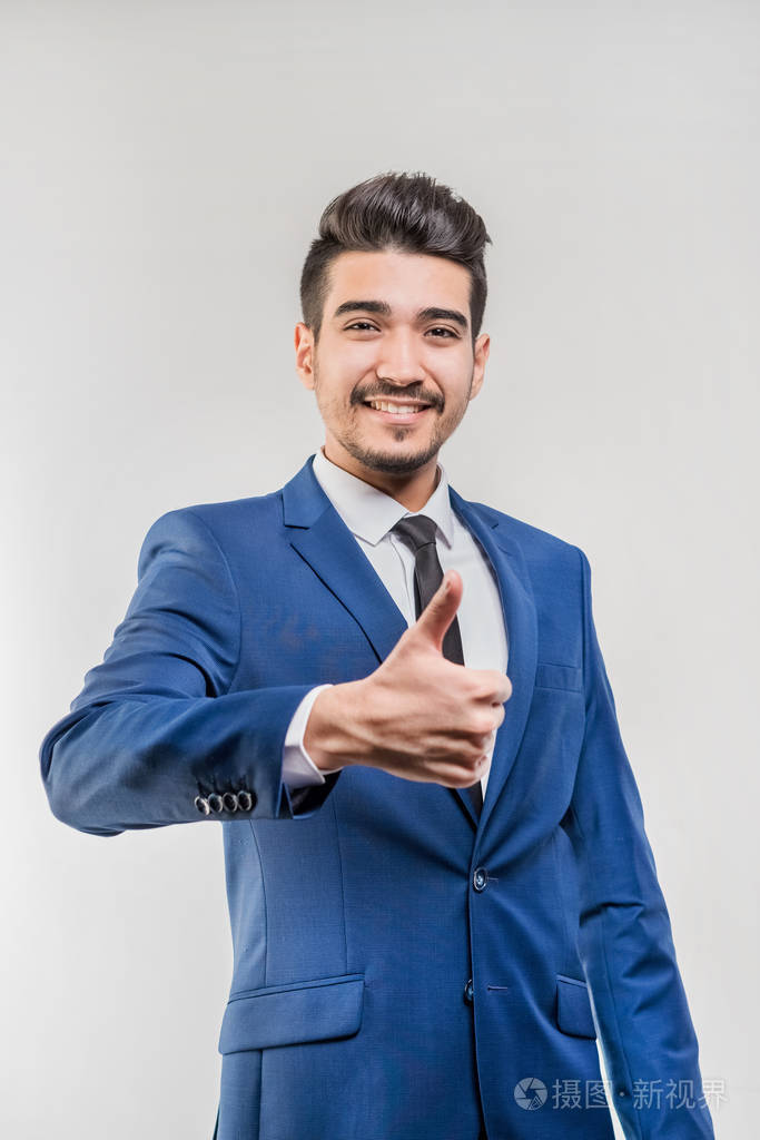 年轻迷人的男人穿着蓝色西装在灰色背景上竖起大拇指孤立