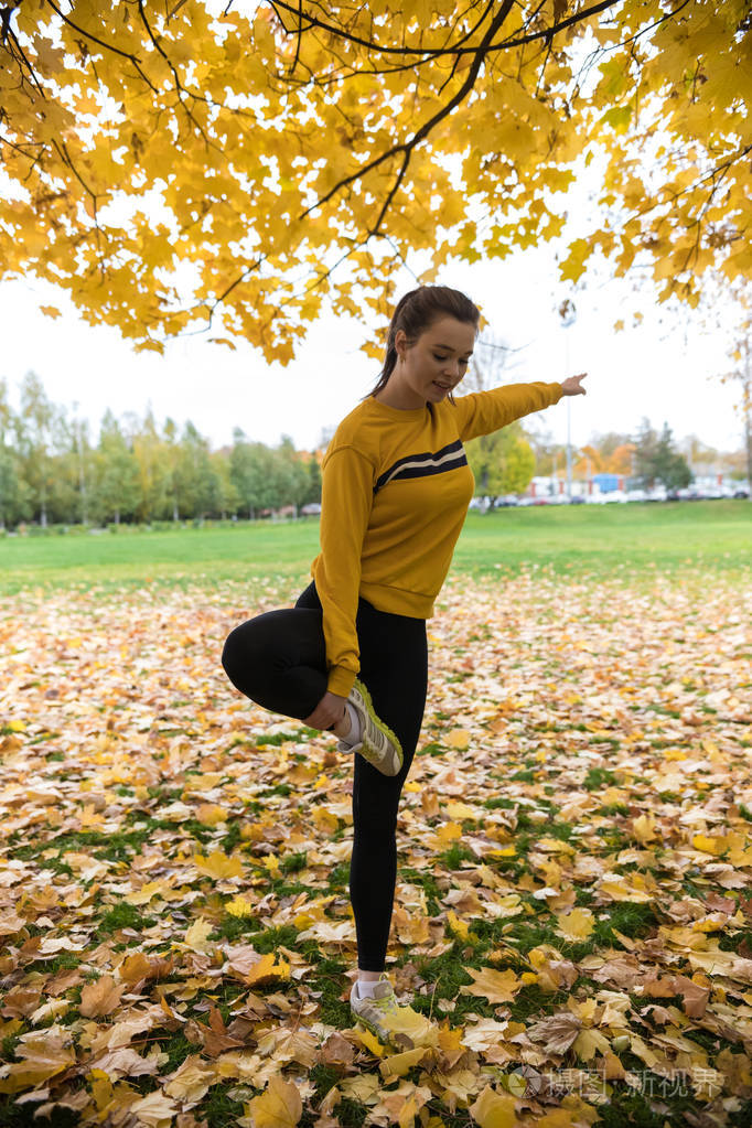 秋季照片的运动妇女伸展在森林在早晨与树木的背景.单腿停留
