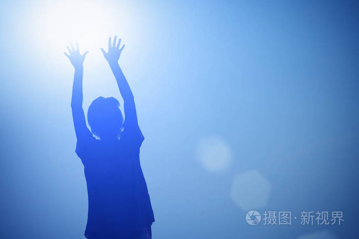 一个女孩的剪影在蓝色背景上举起双手对着太阳