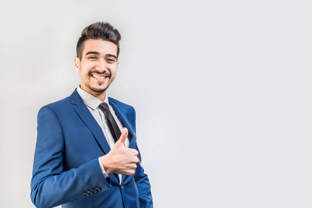 年轻迷人的男人穿着蓝色西装,在灰色背景上竖起大拇指.孤立照片