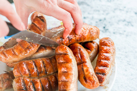 s hand with a knife cuts sausage on the grill