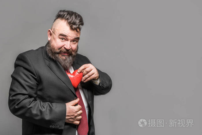 穿着红色领带的成年胡须男人从夹克里掏出红色的心灰色背景